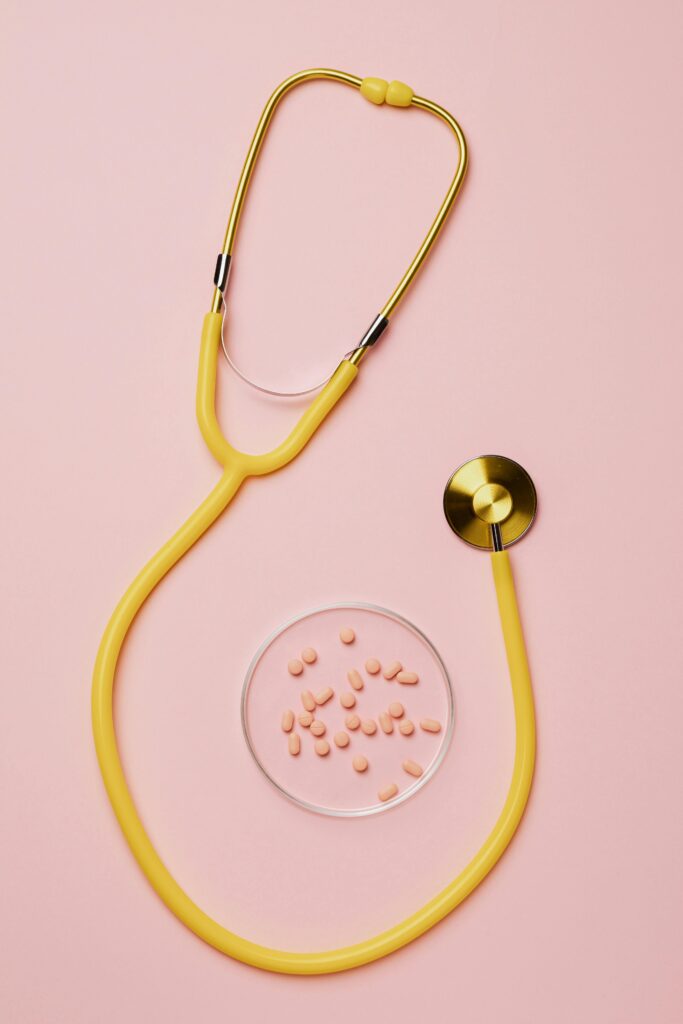 Flat lay of yellow stethoscope with pink pills on a pastel pink background.